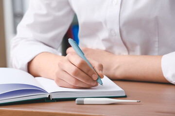 Female doctor writing in notebook at table in clinic, closeup