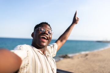 Ecstatic African American man taking selfie at the beach during vacations. Happy, black male looking at camera.
