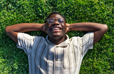 Top view of black man relaxing on grass. Happy black male lying on grass, smiling, enjoying life.