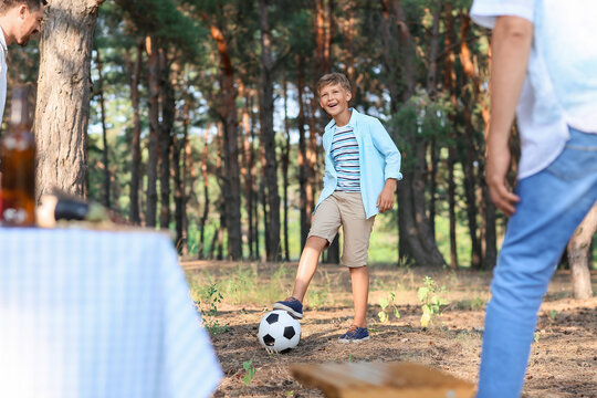 Little boy playing soccer with his father and grandfather in forest