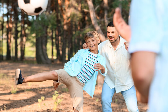 Little boy playing soccer with his father in forest