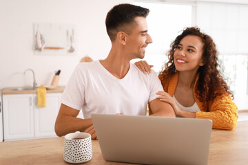 Young couple with laptop sitting at table in kitchen