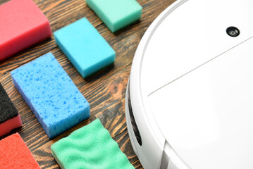 Robot vacuum cleaner and different sponges on wooden background, closeup