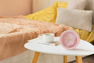 Coffee table with alarm clock, jar of cream and newspaper in bedroom