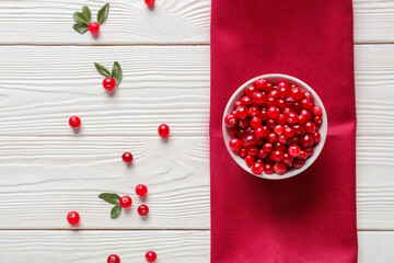 Bowl with red lingonberries and napkin on white wooden background