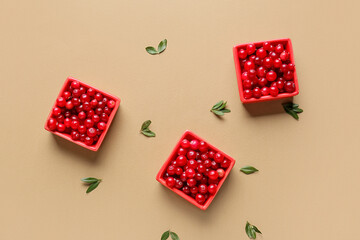 Bowls with red lingonberries and leaves on beige background