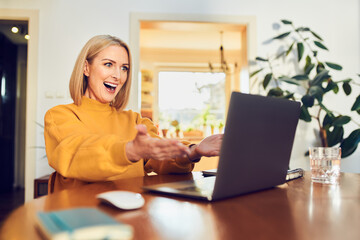 Winning happy middle aged woman celebrating success looking on laptop at home