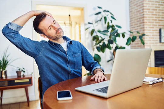 Man stretching his neck while working on laptop at home