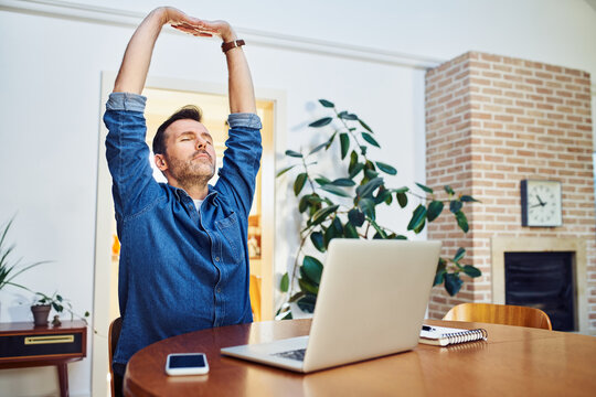 Man stretching his arms while working on laptop at home