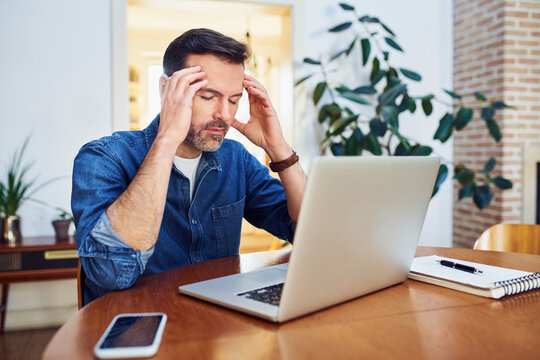 Thoughtful worried man working from home sitting at a table with closed eyes