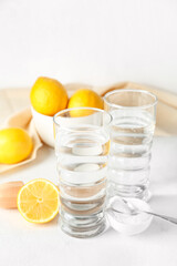 Glasses of water, bowl with baking soda and ripe lemons on light background