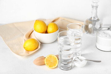 Glasses of water, bowl with baking soda and ripe lemons on light background