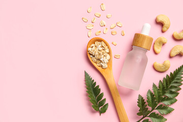 Bottle of natural serum, spoon with oat flakes, fern leaves and cashew nuts on pink background