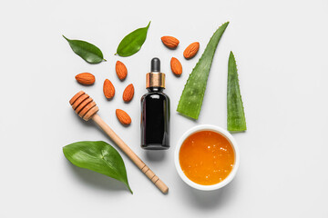 Bottle of natural serum with plant leaves, spoon, honey and almond nuts on light background