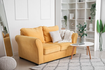 Interior of light living room with yellow sofa and eucalyptus in vase