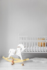 Baby crib and rocking horse with cubes near light wall