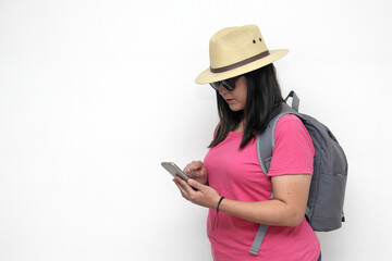 Latin adult woman with sunglasses, hat and pink shirt uses her cell phone to locate herself on a map app as a tourist while discovering a new place on vacation
