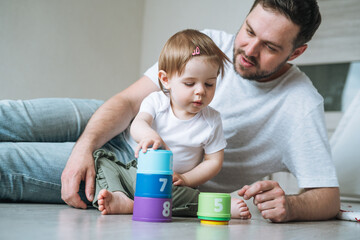 Happy father young man and baby girl little daughter having fun playing with toy in children room at home