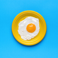 Fresh fried egg in a yellow plate on a blue background. A popular breakfast. Minimal concept. A popular breakfast.