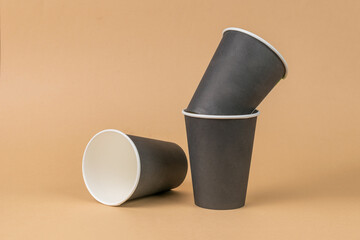 Three dark paper cups on a light brown background. Minimal concept.