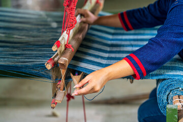 Craftsmen of Thai indigo cotton. Hand of young woman weaving silk in traditional way at manual loom.