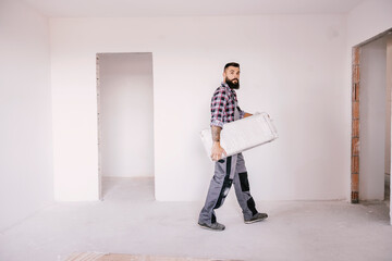 A strong blue collar worker relocating material in an apartment in building process.