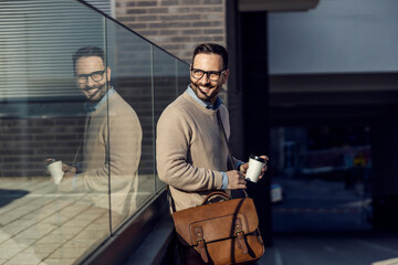 A pleased smart casual man leaning on the glass and drinking a coffee.