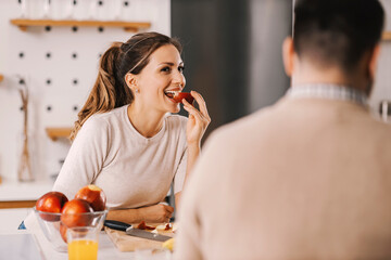 A woman eating apple in kitchen at home and smiling at boyfriend.