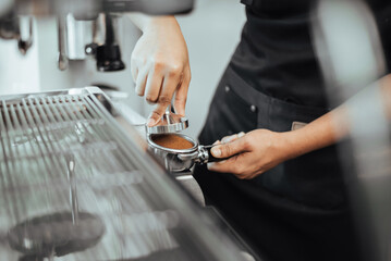 Barista using a tamper to press ground coffee into a portafilter. Close-up view on barista hands to making coffee with coffee machine. Coffee owner concept.
