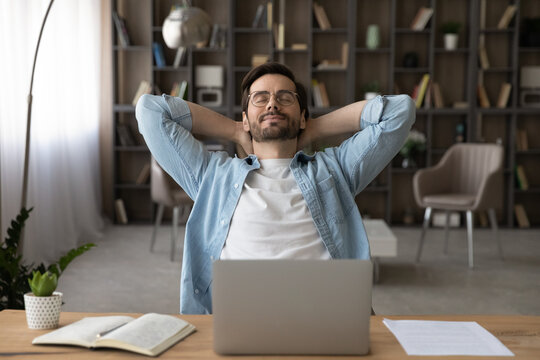 Meeting friday. Happy young guy freelancer enjoy calm moment when task is done relax rest stretch back hold hands over head. Serene millennial man recline on chair with closed eyes take break in work