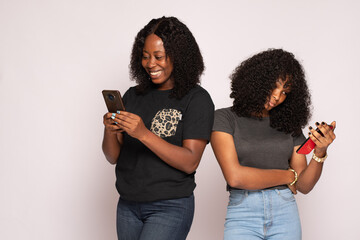 two african girls check their phones, one is happy the other is sad