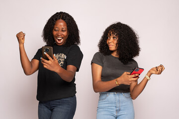 two african girls checking their phones, one is happy the other is sad