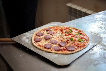 food cooking, culinary and people concept - cook or baker hand with pizza on peel at pizzeria