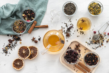 A set of different varieties of Chinese herbal and green tea in a glass dish and a kettle with hot tea on a light background. View from above. Herbal treatment. Healthy lifestyle.