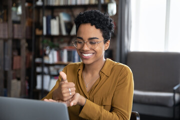 African woman teach learner via video call on laptop sit at desk show symbols with hands use...
