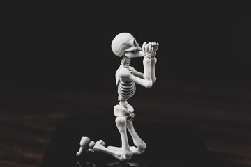 Pray skeleton figurine. Prayer figure on knees on dark background