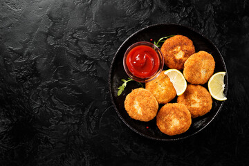 Chicken patties or fish cakes fried in breadcrumbs with ketchup and lemon slices. Black  background, top view	