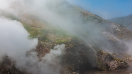 The hillside is shrouded in thick steam from an erupting geyser. Poor visibility due to haze. Kamchatka. Valley of Geysers