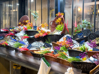 Paris, France - April 7, 2022: Fresh fish in ice baskets beautiful decorated. A fish market stall display at a shopping area in Paris. Colorful artificial flowers decorating the seafood 