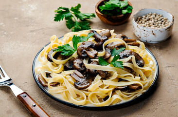Cooked pasta with mushrooms with parsley on plate on beige stone kitchen table background, top view. Vegan cooking and eating, italian cuisine recipe