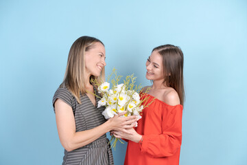 Fototapeta na wymiar Portrait charming pretty attractive mother and daughter with big bouquet of aromatic flowers happy smiling in red and gray dresses, isolated on blue background. Family and togetherness concept