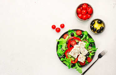 Greek salad with feta cheese, olives, cherry tomato, paprika, cucumber and red onion, healthy vegeterian mediterranean diet food, low calories eating. White stone background, top view