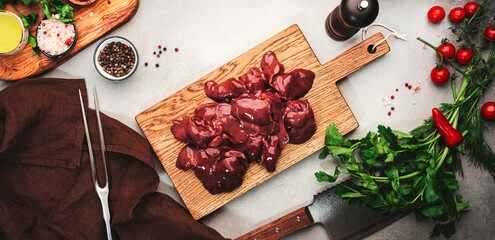 Fresh raw chicken liver on cutting board and ingredients for cooking on concrete white stone...
