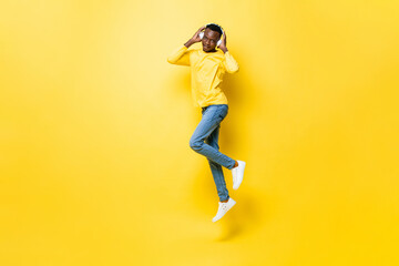 Fototapeta na wymiar Young African man listening to music on headphones and jumping in isolated yellow studio background
