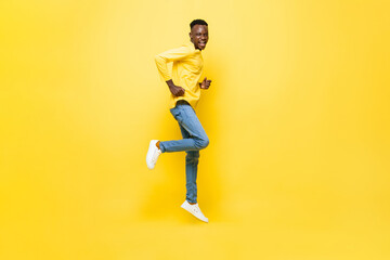 Fototapeta na wymiar Full length portrait of excited African man jumping in isolated yellow color studio background