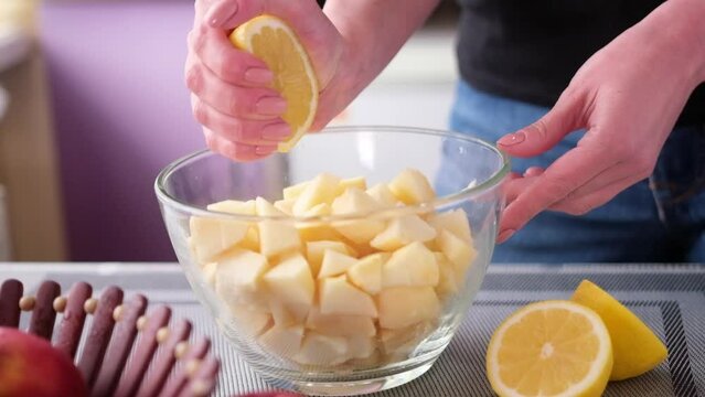 Apple pie preparation series - woman squeezing lemon juice into glass bowl with chopped apples