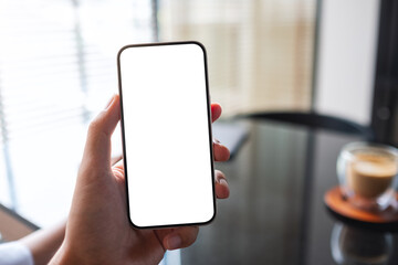 Mockup image of a man holding mobile phone with blank white screen with coffee cup on the table