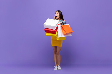 Surprised Asian woman carrying colorful shopping bags in purple color studio background