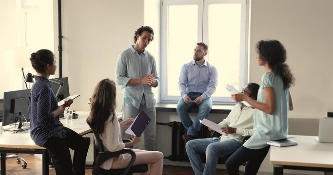 Smart Latin male team member speak to multiracial group offer marketing plan propose idea share skills on corporate briefing. Young man business coach hold conversation with diverse corporate staff