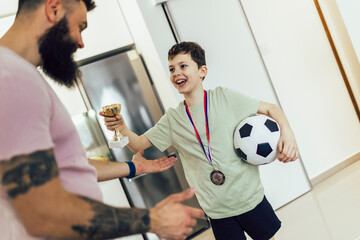 Proud father feel so excited to see his son medal and trophy in his hand after football tournament.